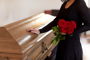 woman holding flowers with hand on coffin at funeral