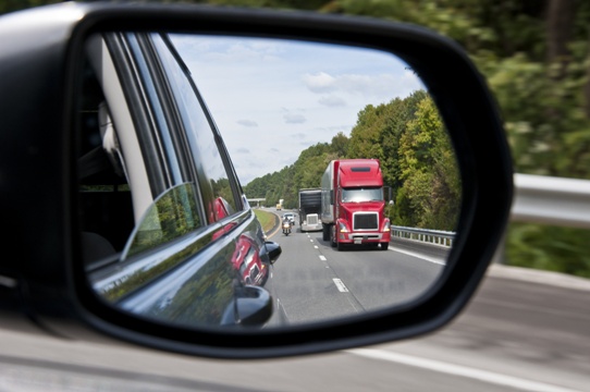 motorcycle next to semi truck on highway seen in rearview mirror