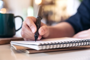 person taking notes in notebook next to coffee mug