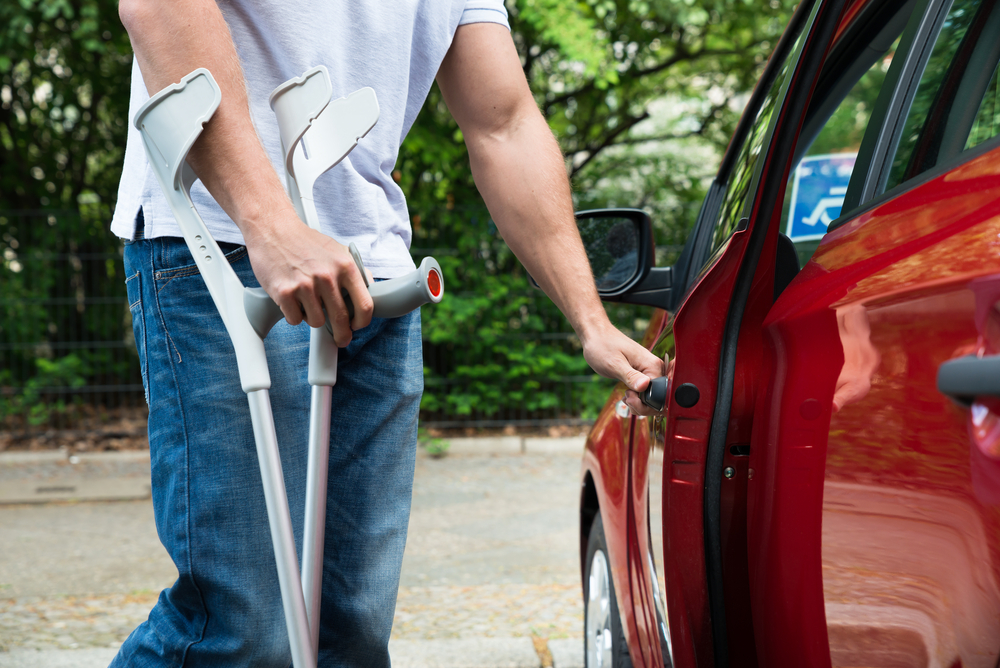 Man with crutch opening a car door